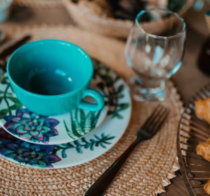 A cozy breakfast setup featuring a teal teacup, plate with floral design, and freshly baked croissants on a woven placemat.