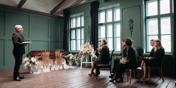 A peaceful indoor funeral ceremony scene with a pastor and seated mourners.