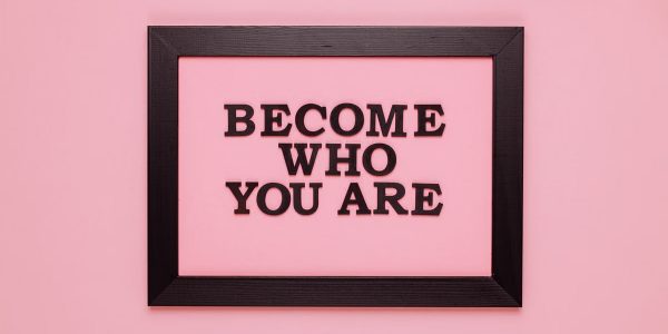 Inspiring quote 'Become Who You Are' framed on a vibrant pink wall, perfect for encouragement.